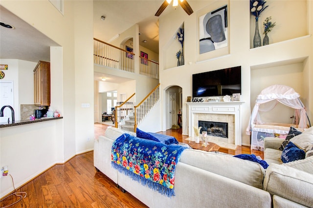 living area featuring a ceiling fan, wood finished floors, a high ceiling, stairs, and a premium fireplace