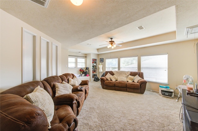 carpeted living room with a textured ceiling, a tray ceiling, visible vents, and ceiling fan