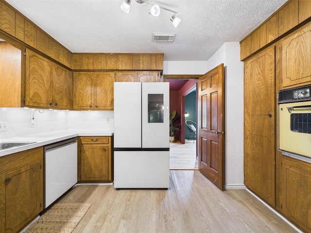 kitchen featuring brown cabinetry, white appliances, and light wood-style flooring