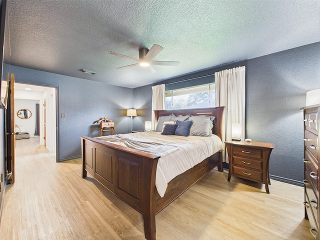 bedroom with a textured ceiling, a textured wall, visible vents, and light wood-type flooring