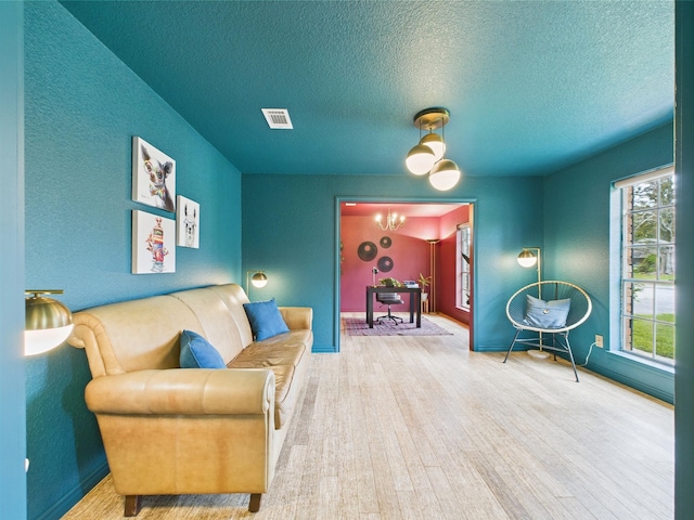 living area featuring a notable chandelier, a textured ceiling, baseboards, wood finished floors, and visible vents
