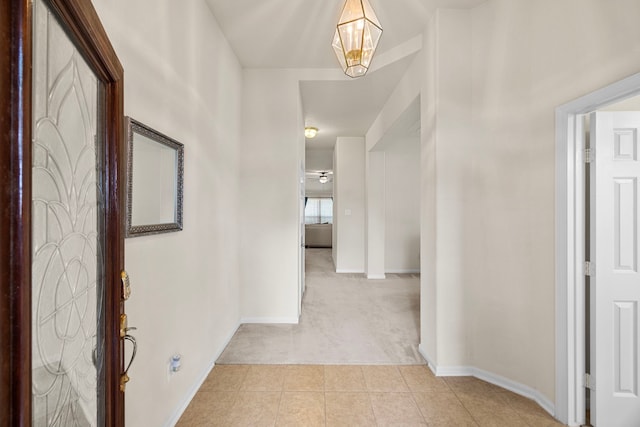 corridor featuring light tile patterned floors, baseboards, and light carpet