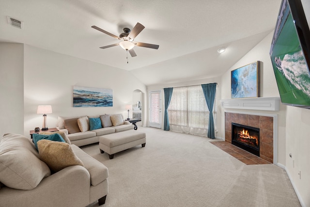 carpeted living room featuring ceiling fan, visible vents, arched walkways, a tile fireplace, and vaulted ceiling