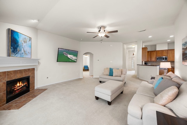 living room with ceiling fan, light colored carpet, recessed lighting, a tile fireplace, and arched walkways