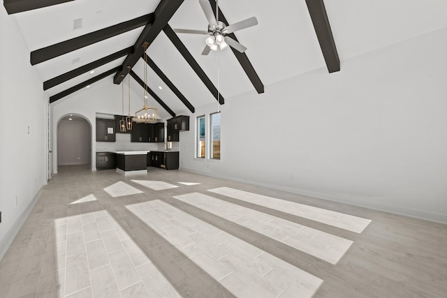 unfurnished living room featuring arched walkways, beamed ceiling, ceiling fan with notable chandelier, and high vaulted ceiling