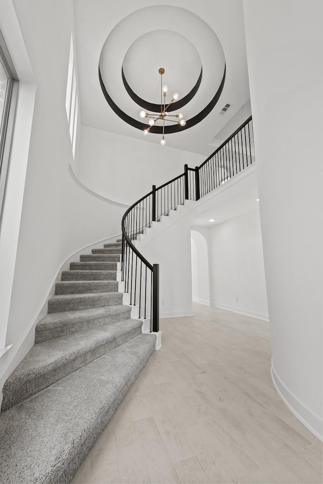 staircase featuring visible vents, baseboards, a high ceiling, and a chandelier