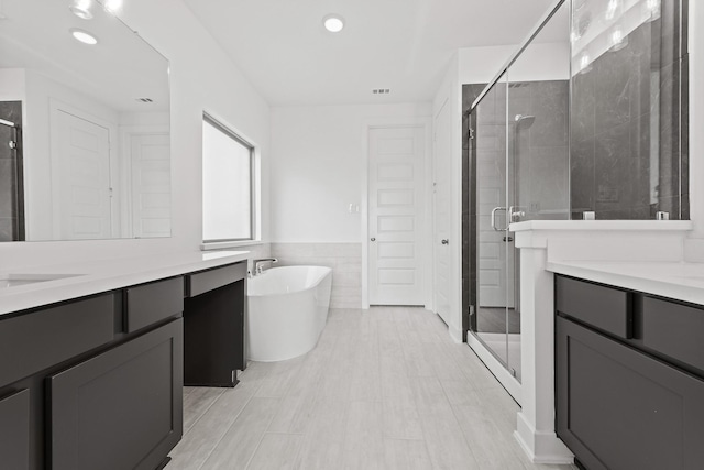 full bath with a freestanding bath, vanity, a wainscoted wall, tile walls, and a shower stall