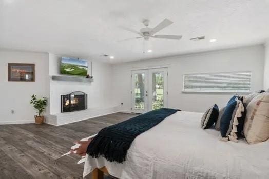 bedroom featuring wood finished floors, baseboards, a warm lit fireplace, access to outside, and french doors