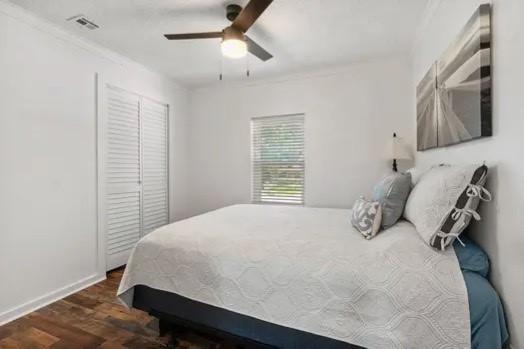 bedroom with ceiling fan, visible vents, wood finished floors, baseboards, and a closet