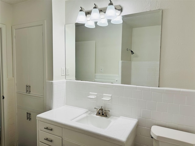 bathroom featuring vanity, a wainscoted wall, toilet, and tile walls