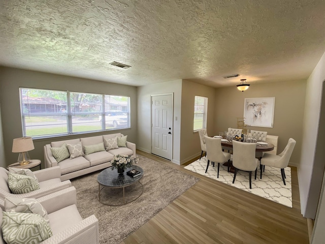 living room with visible vents, baseboards, a textured ceiling, and wood finished floors