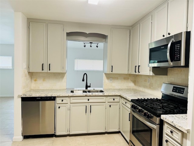 kitchen featuring light stone counters, a sink, stainless steel appliances, decorative backsplash, and light tile patterned floors
