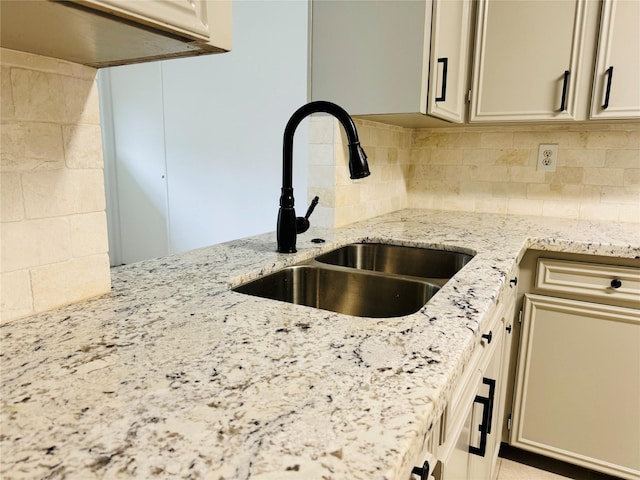 details featuring backsplash, light stone counters, and a sink