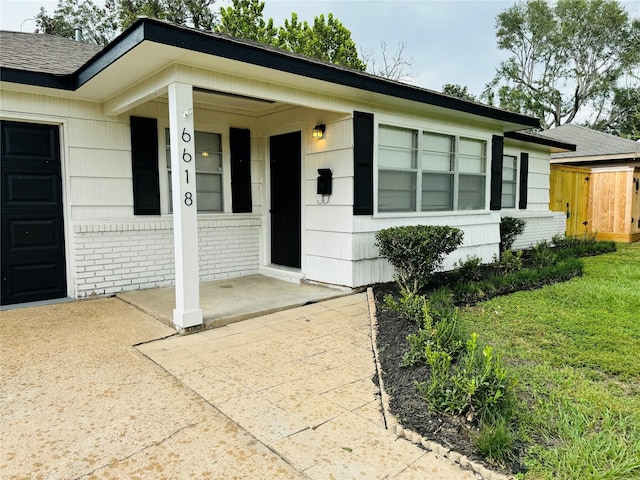 doorway to property featuring a lawn, brick siding, and covered porch
