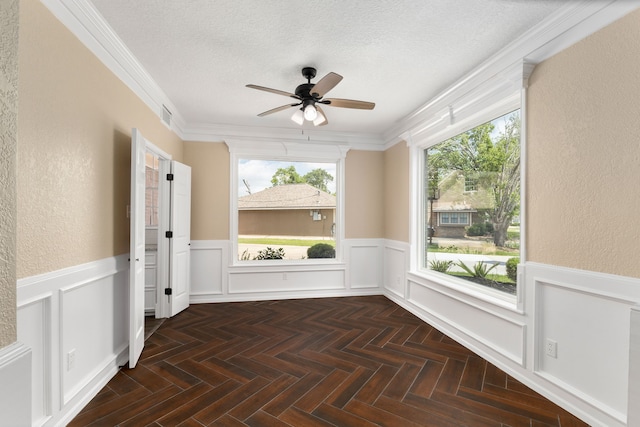spare room with a textured ceiling, visible vents, ceiling fan, and a wainscoted wall