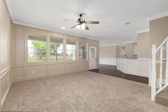 unfurnished living room featuring dark colored carpet, ornamental molding, a ceiling fan, and a decorative wall