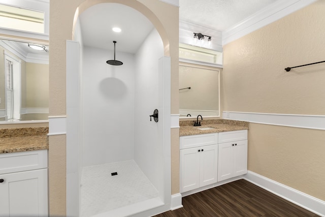 full bathroom with vanity, crown molding, a textured wall, wood finished floors, and tiled shower