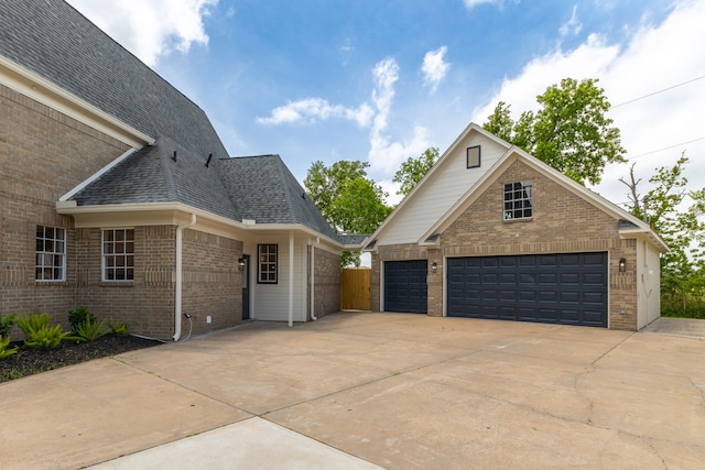 exterior space with brick siding, roof with shingles, and driveway