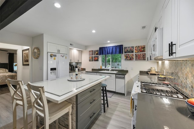 kitchen with a sink, light wood-style floors, a breakfast bar, white appliances, and white cabinetry