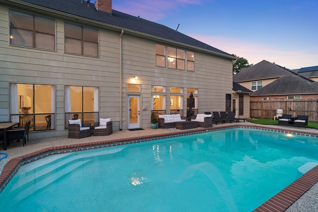 pool at dusk with an outdoor hangout area, a patio, and fence