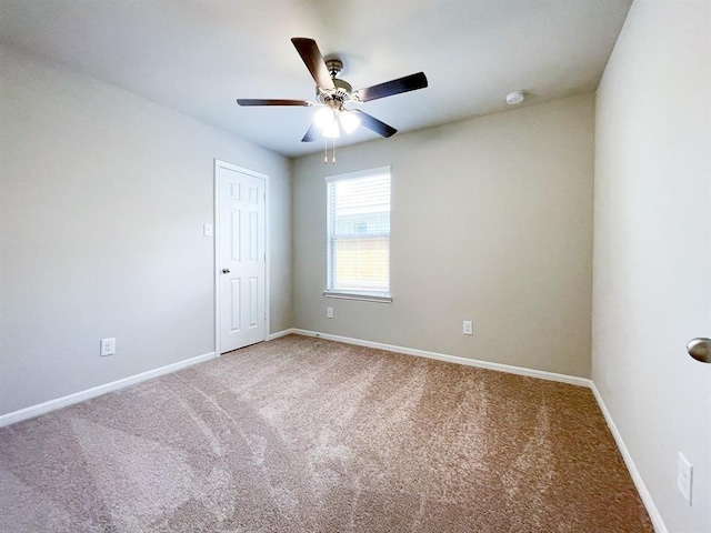 carpeted spare room featuring baseboards and a ceiling fan