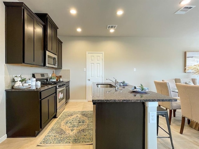 kitchen featuring stainless steel appliances, visible vents, a center island with sink, and a sink