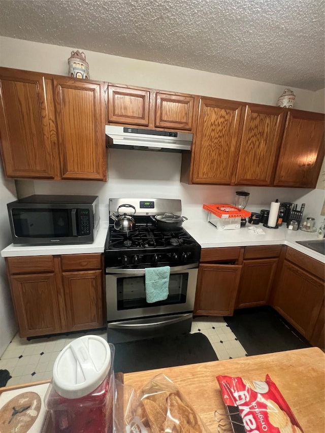 4710 Salina St, Houston, TX 77026 - kitchen with stainless steel gas range, under cabinet range hood, light floors, light countertops, and brown cabinetry