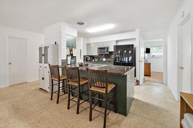 kitchen with black fridge with ice dispenser, a peninsula, light speckled floor, stainless steel microwave, and tasteful backsplash