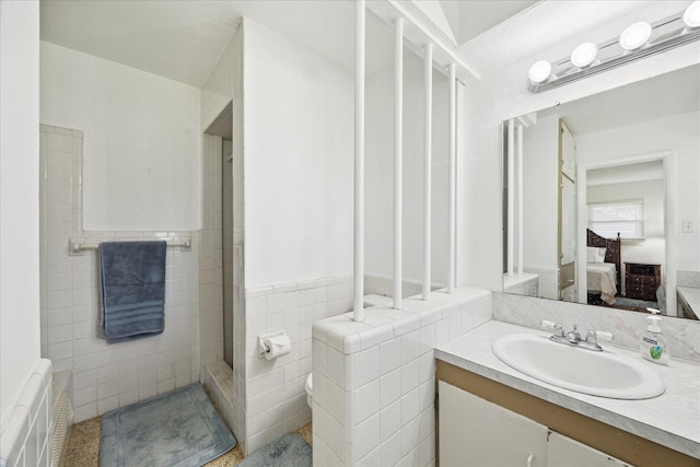 ensuite bathroom featuring wainscoting, a tile shower, vanity, tile walls, and ensuite bathroom