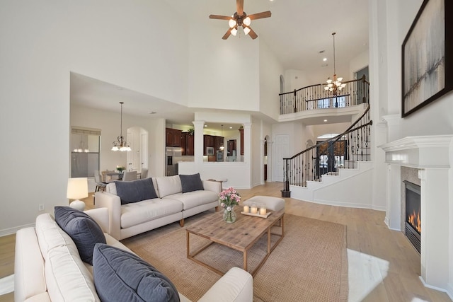 living area with light wood-type flooring, stairway, ceiling fan with notable chandelier, a high ceiling, and a premium fireplace