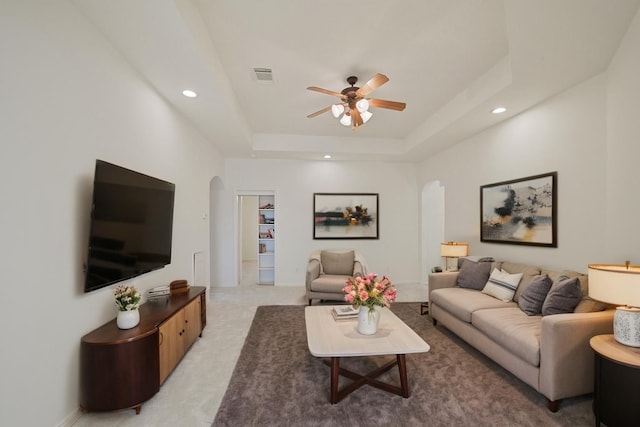 living room with a ceiling fan, visible vents, arched walkways, a tray ceiling, and recessed lighting