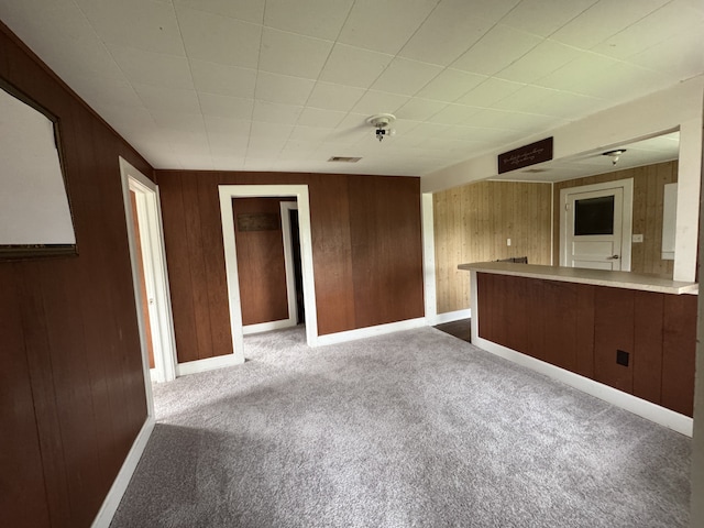 interior space with carpet flooring, wood walls, visible vents, and baseboards