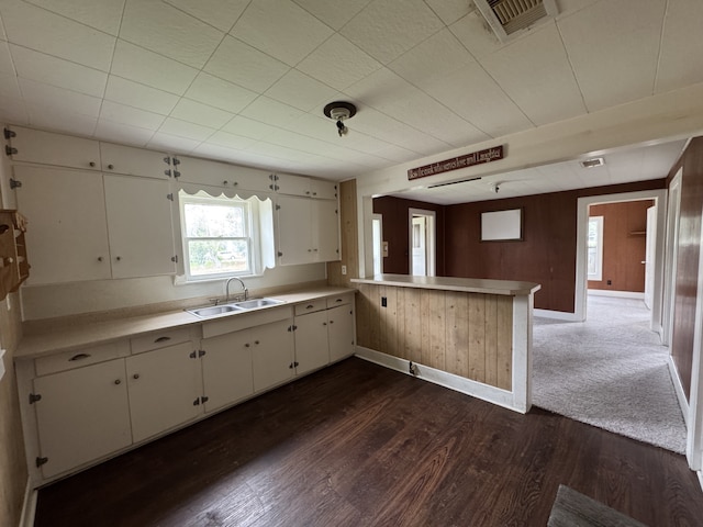 kitchen with a sink, light countertops, dark wood finished floors, a peninsula, and baseboards