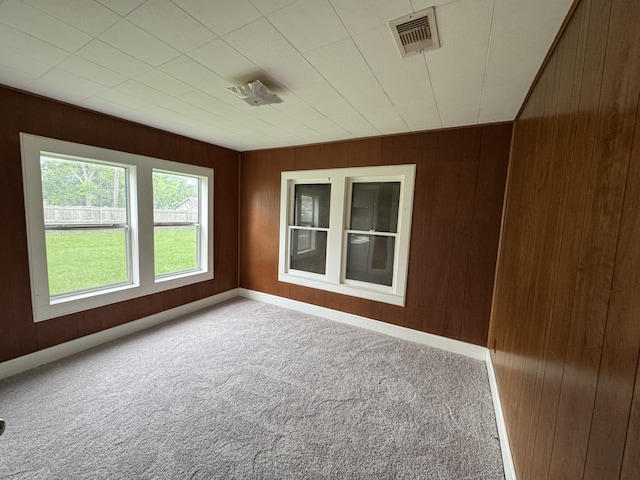 carpeted empty room with wooden walls, baseboards, and visible vents