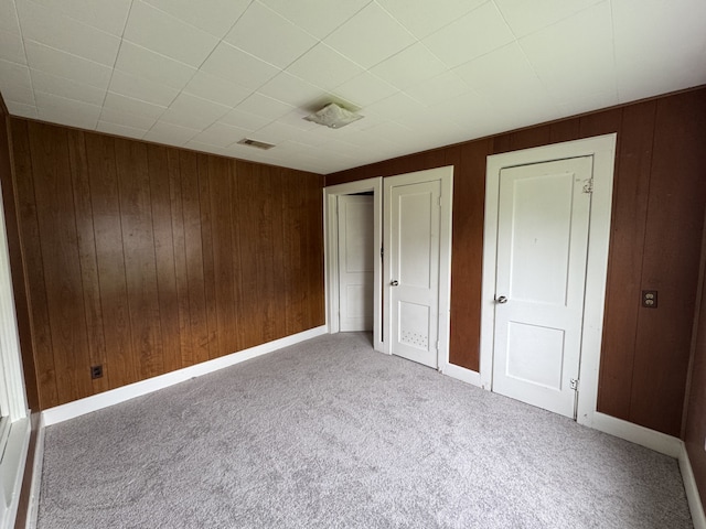 unfurnished bedroom with visible vents, wood walls, carpet, and baseboards