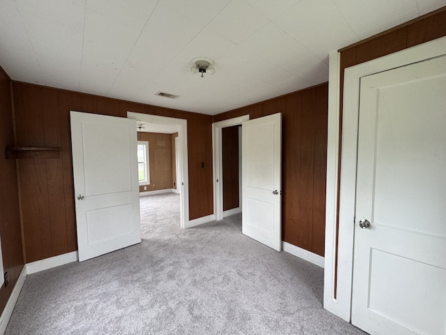 unfurnished bedroom featuring visible vents, wood walls, baseboards, and carpet floors