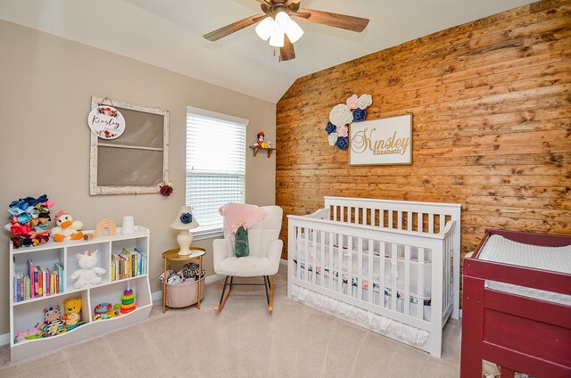 carpeted bedroom with a crib, ceiling fan, vaulted ceiling, and wood walls