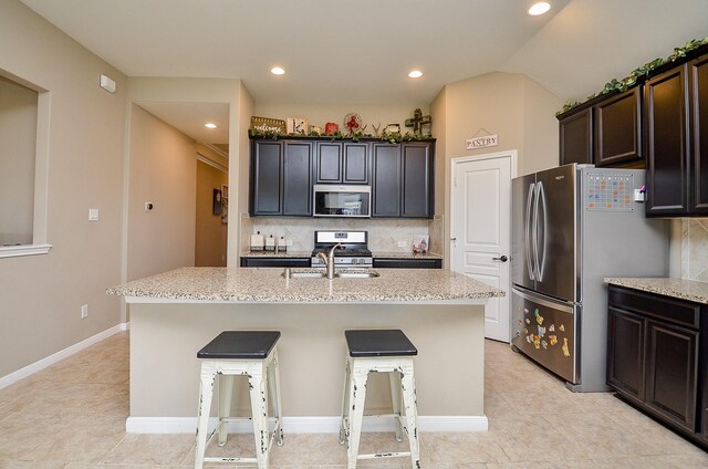kitchen with light stone counters, appliances with stainless steel finishes, backsplash, and an island with sink