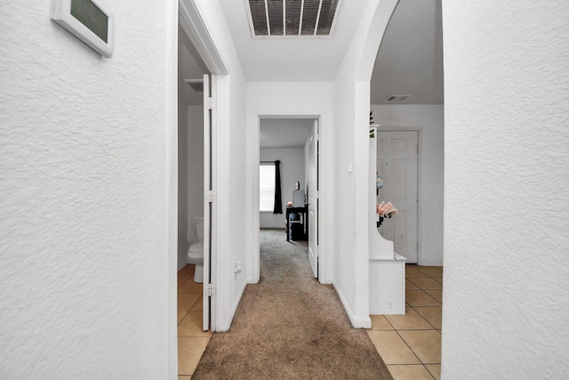 corridor with visible vents, arched walkways, a textured wall, and light tile patterned floors