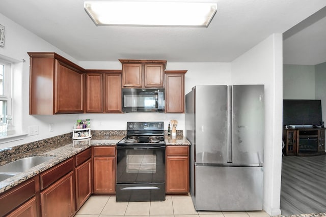 kitchen featuring dark stone counters, light tile patterned floors, a sink, and black appliances