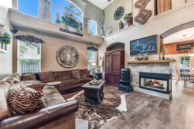living room with arched walkways, a tile fireplace, wood finished floors, and a towering ceiling