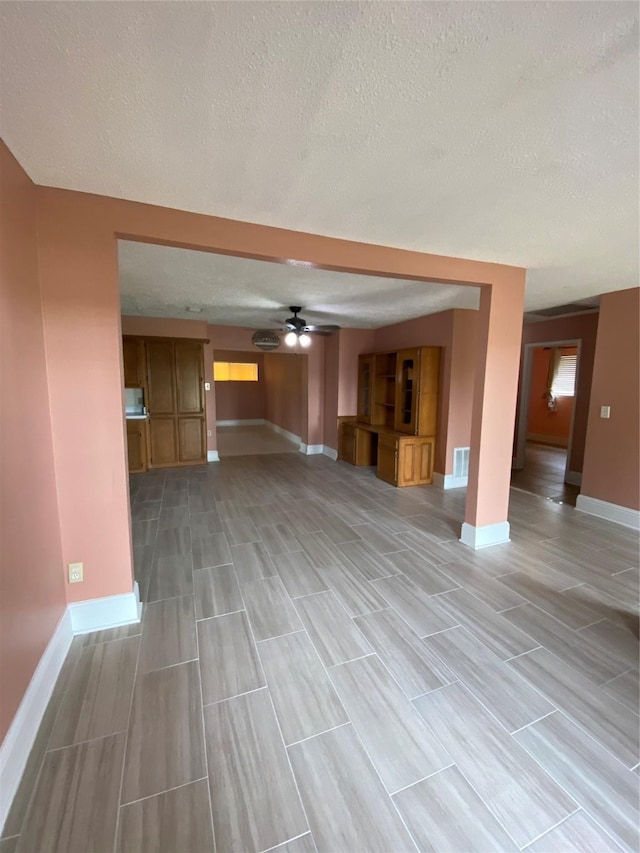 unfurnished living room with baseboards, a textured ceiling, ceiling fan, and visible vents