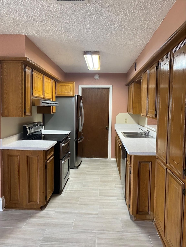 kitchen featuring light countertops, a textured ceiling, under cabinet range hood, a sink, and appliances with stainless steel finishes