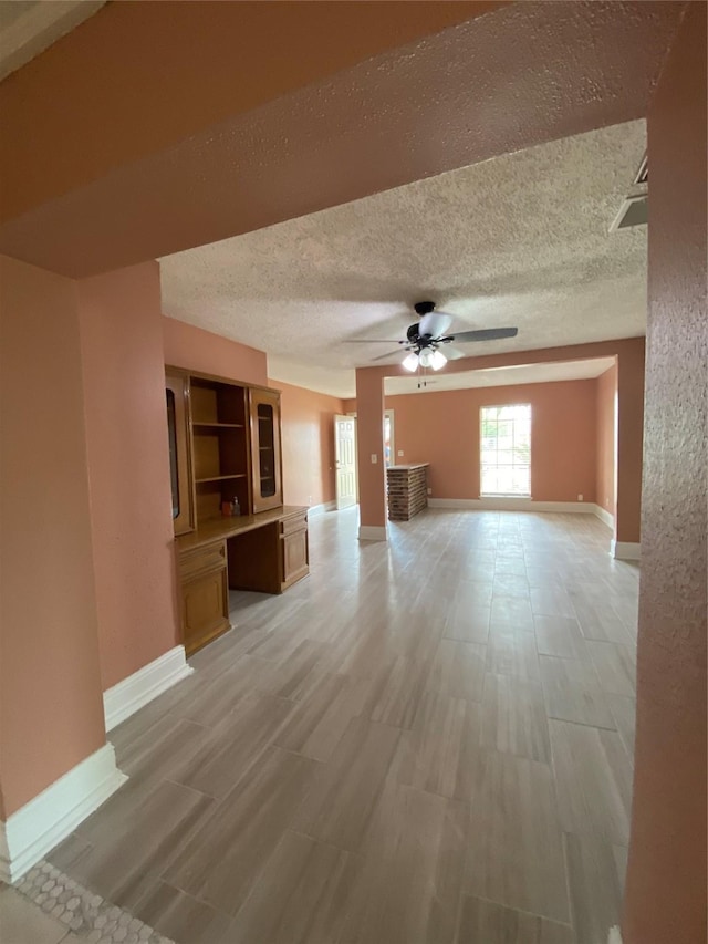 unfurnished living room with baseboards, a ceiling fan, and a textured ceiling