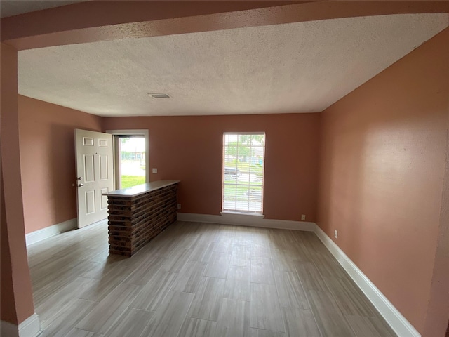interior space featuring a textured ceiling, baseboards, visible vents, and light wood-type flooring