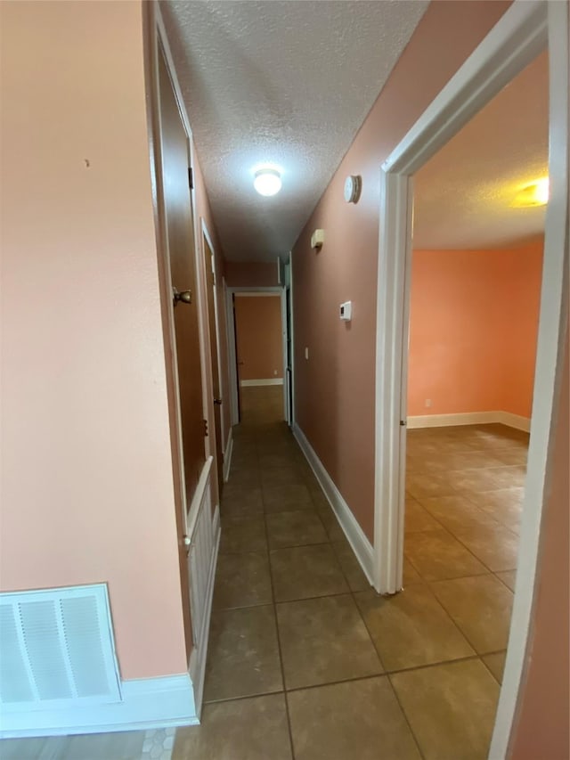 corridor featuring visible vents, baseboards, a textured ceiling, and tile patterned floors