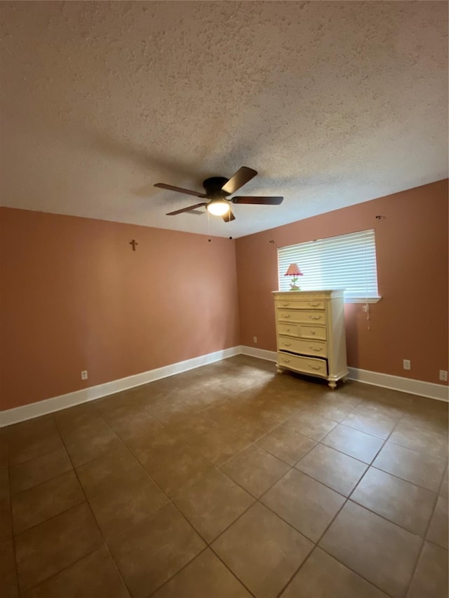 spare room featuring tile patterned floors, ceiling fan, baseboards, and a textured ceiling
