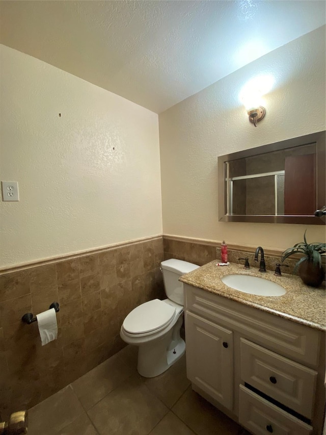 bathroom featuring vanity, toilet, tile walls, a wainscoted wall, and tile patterned floors