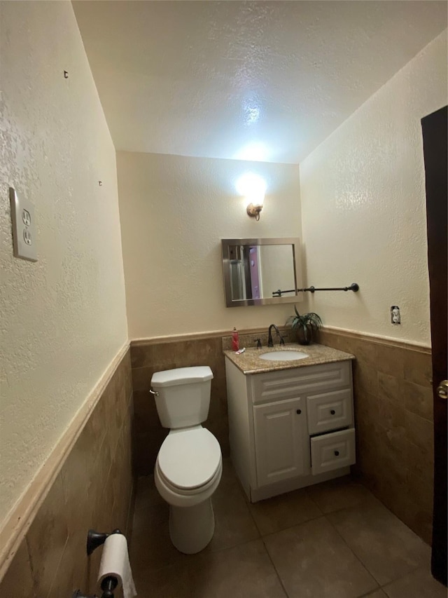 half bathroom featuring toilet, tile walls, tile patterned flooring, and a wainscoted wall