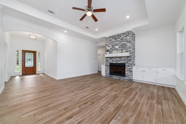 914 Box Elder Dr, Magnolia, TX 77354 - unfurnished living room featuring light wood-style floors, a tray ceiling, a stone fireplace, ceiling fan, and crown molding